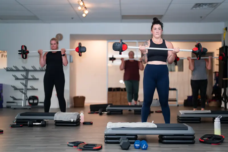Members holding barbells at shoulder height in a strength class