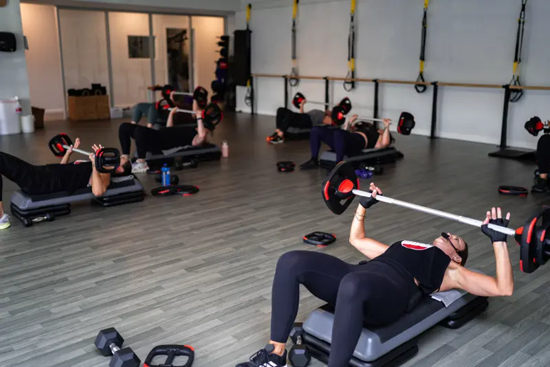 Members doing a barbell chest press on benches in the training room